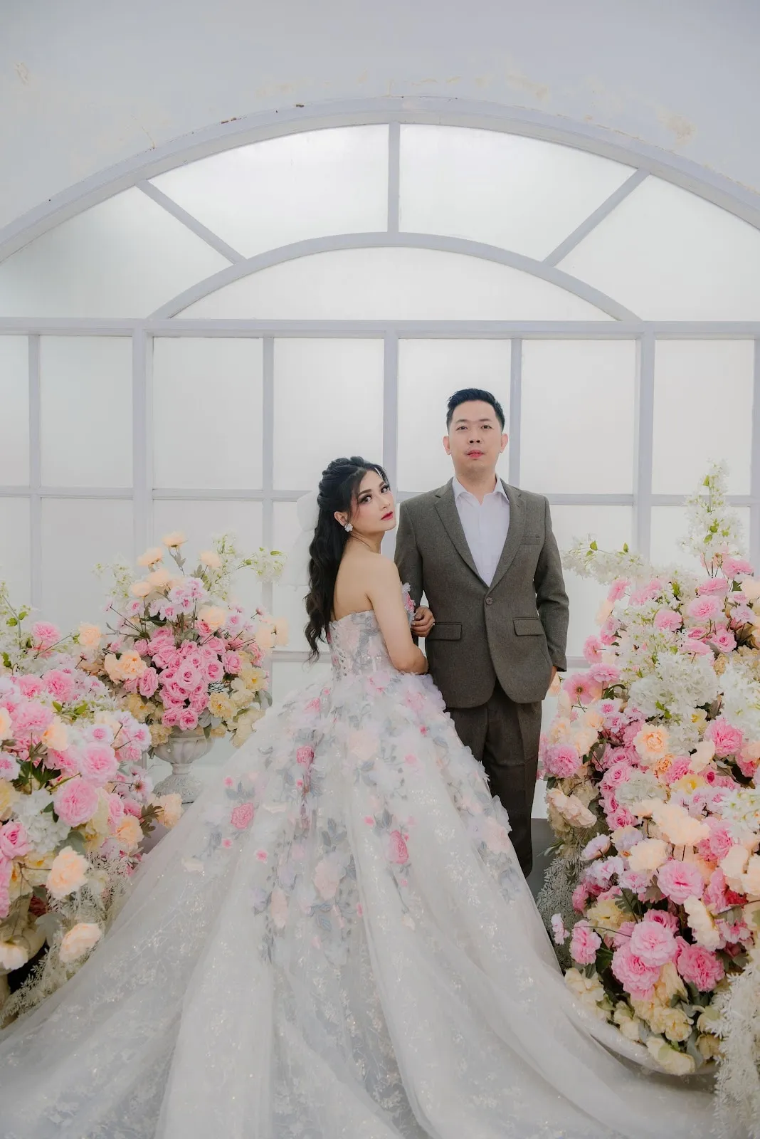 Pasangan pengantin dengan gaun bertabur bunga di depan lengkung bunga