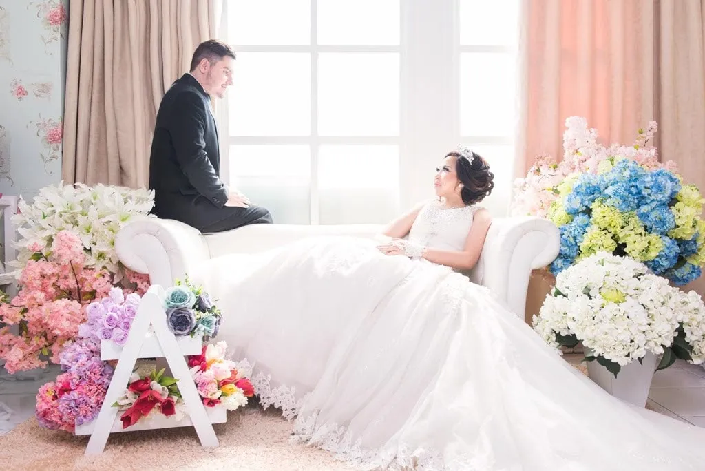 Pasangan pengantin di studio dengan sofa putih dan bunga