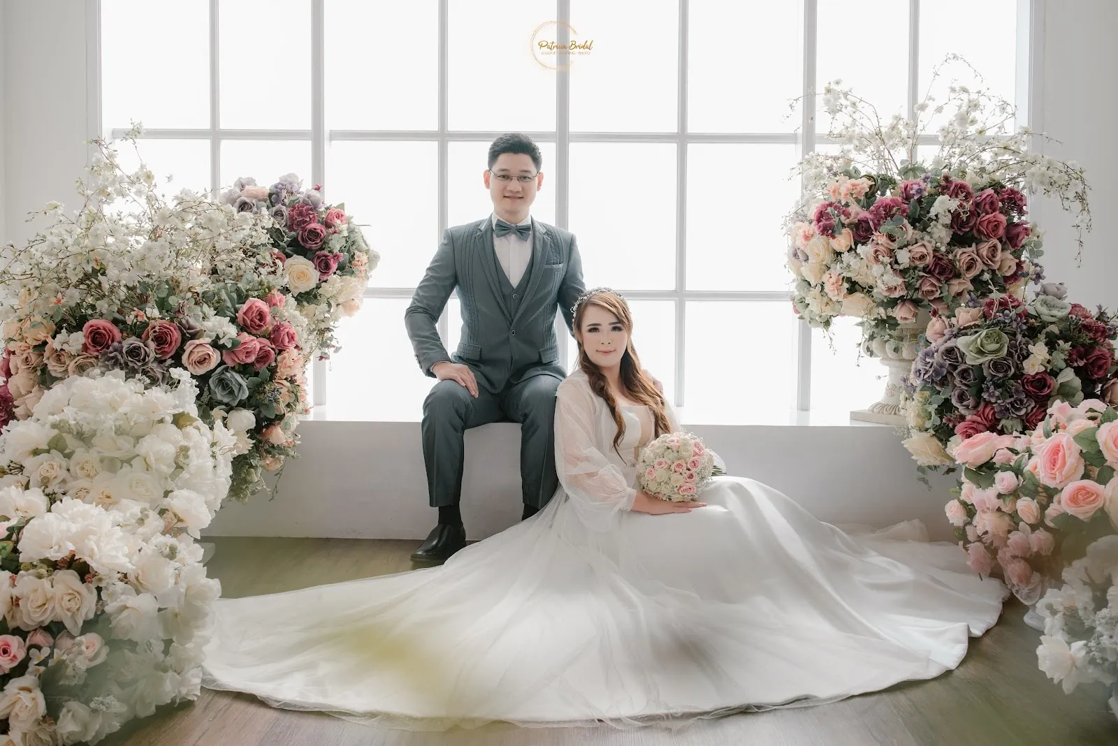 Mempelai pria dengan setelan abu-abu duduk bersama pengantin di studio bunga
