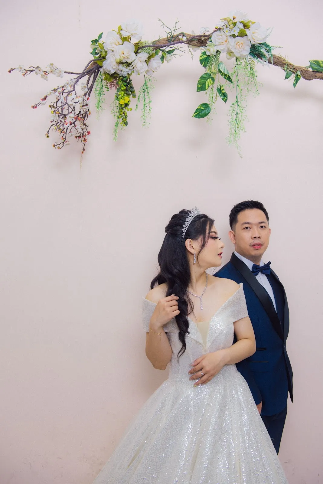 Mempelai pria dengan tuksedo navy dan dasi kupu-kupu di samping pengantin