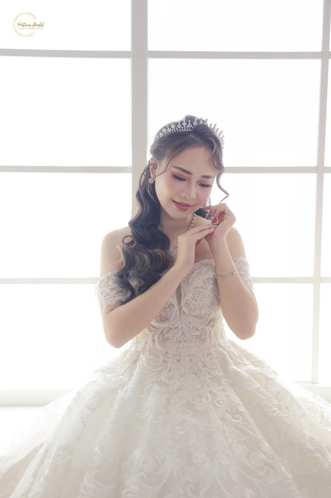 Pengantin mengenakan ball gown renda off-shoulder di depan jendela