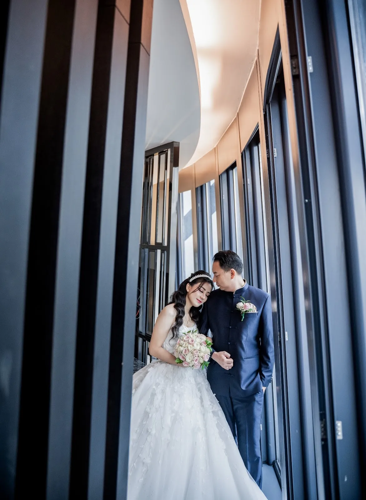 Pasangan pengantin berdiri berdampingan di tepi jendela