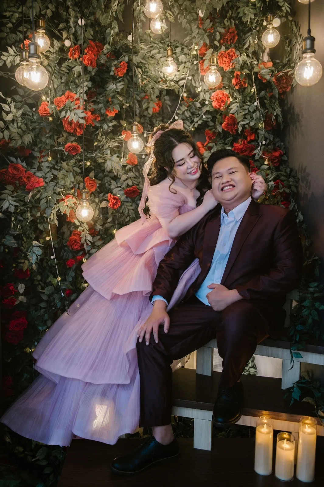 Pasangan prewedding tertawa di dinding mawar, wanita dengan gaun ungu muda