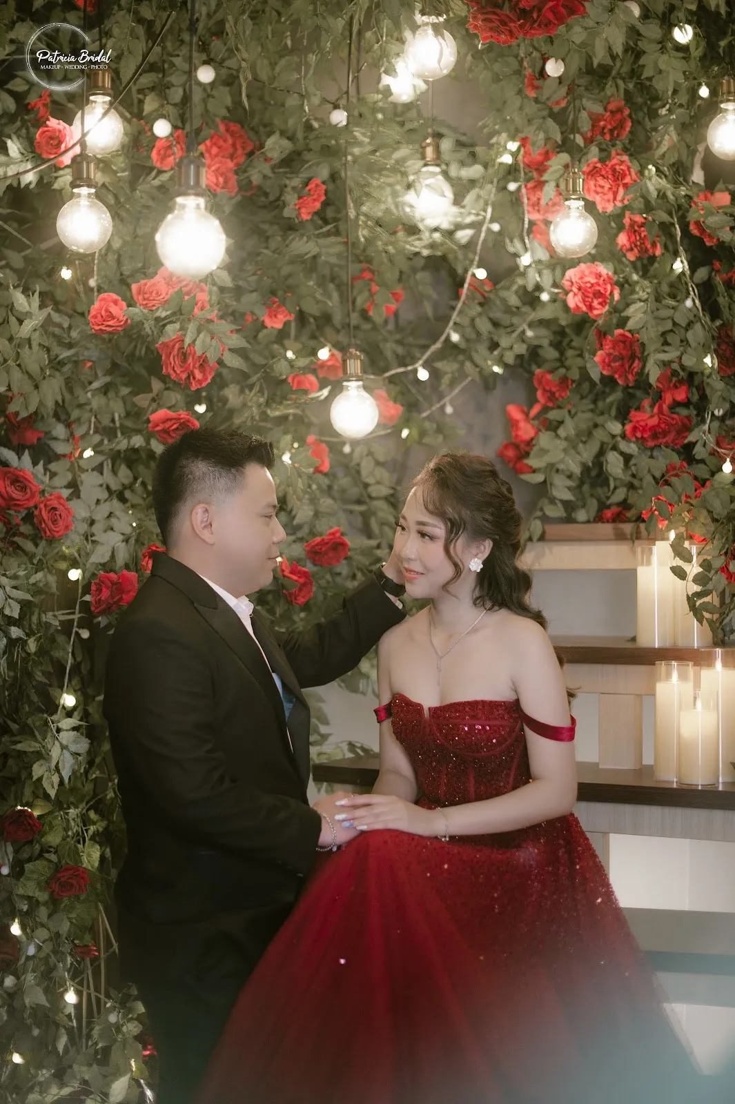 Pasangan prewedding di depan dinding mawar merah dan lampu gantung