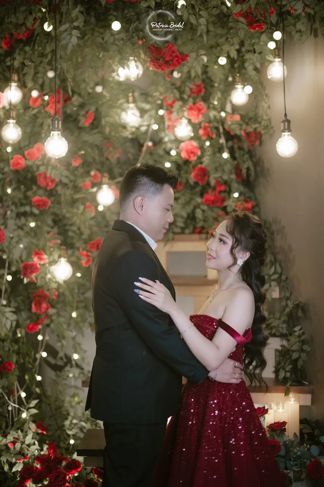 Pasangan prewedding berpelukan di dinding mawar, wanita dengan gaun merah berkilau