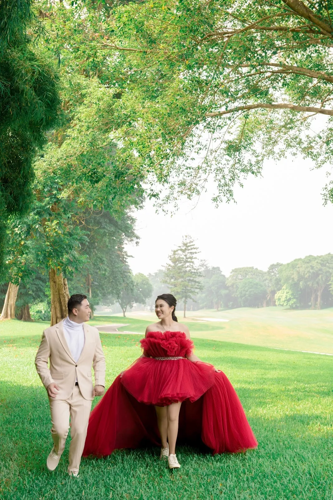 Pasangan prewedding berjalan di taman, wanita dengan gaun merah berekor